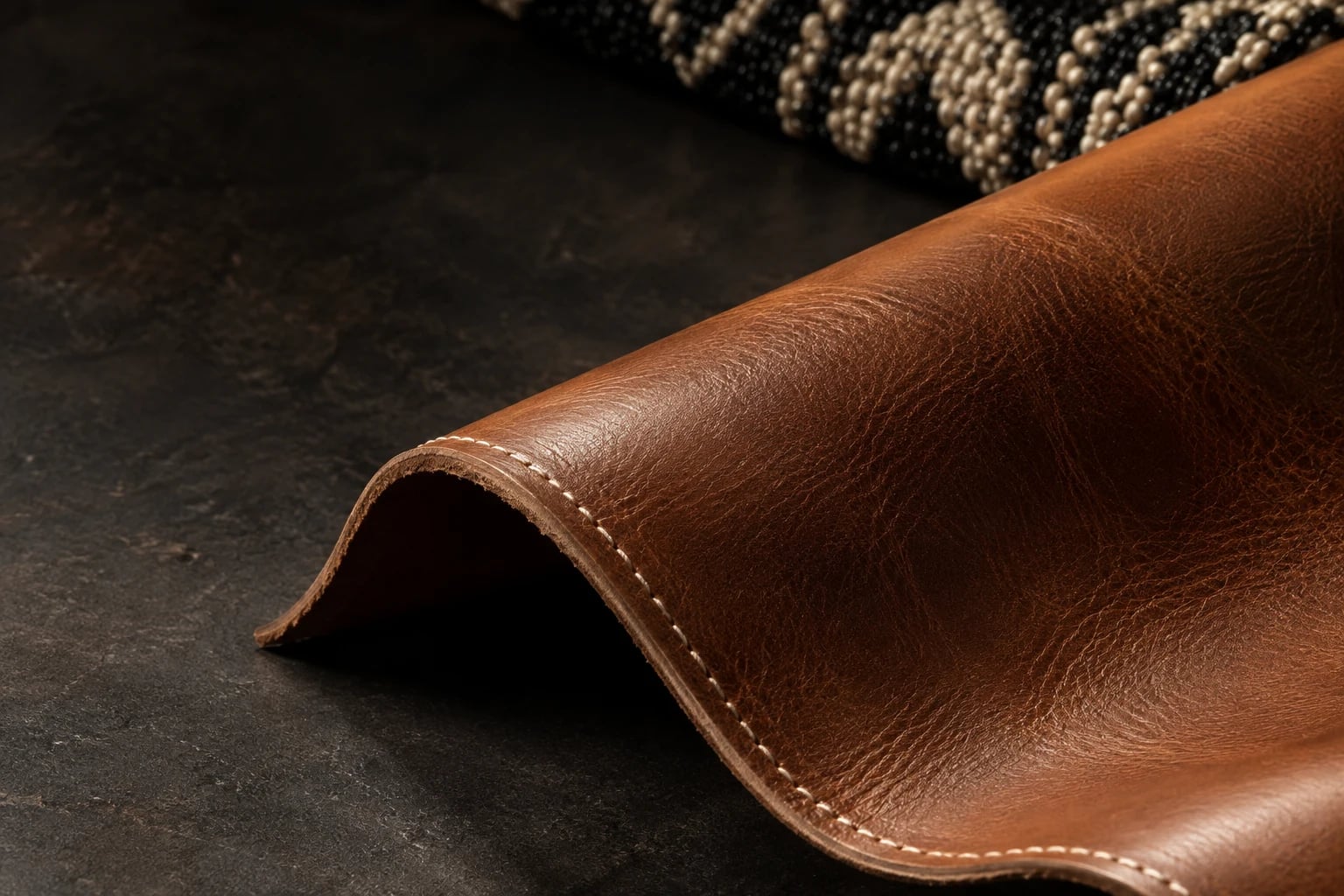 A sculptural fold of cognac leather with cream stitching and a black-and-ivory beaded textile