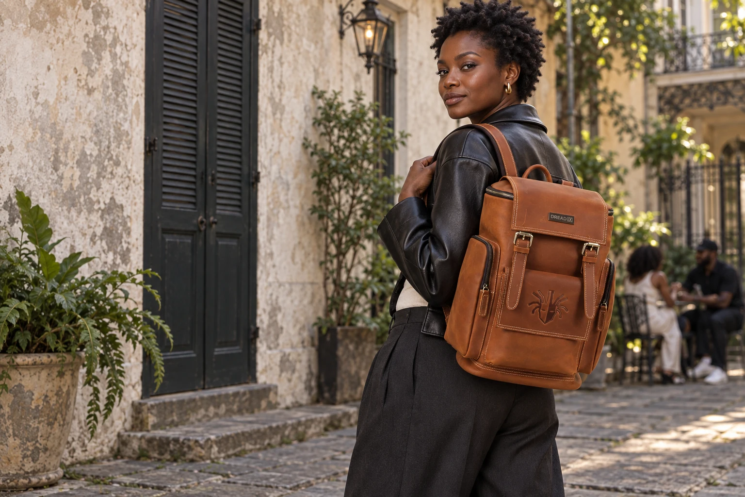 A woman wearing the Classic Brown DREAD IX Backpack in a sunlit New Orleans courtyard